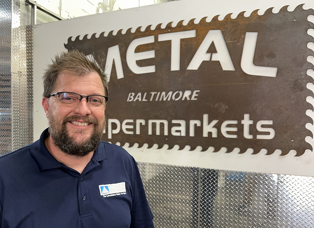 Metal Supermarket owner in front of comapny sign cut out of sheet metal