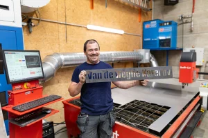 Van de Weghe Karel BV worker standing in front of a Swift-Cut Pro CNC plasma table holding their name cut of sheet metal